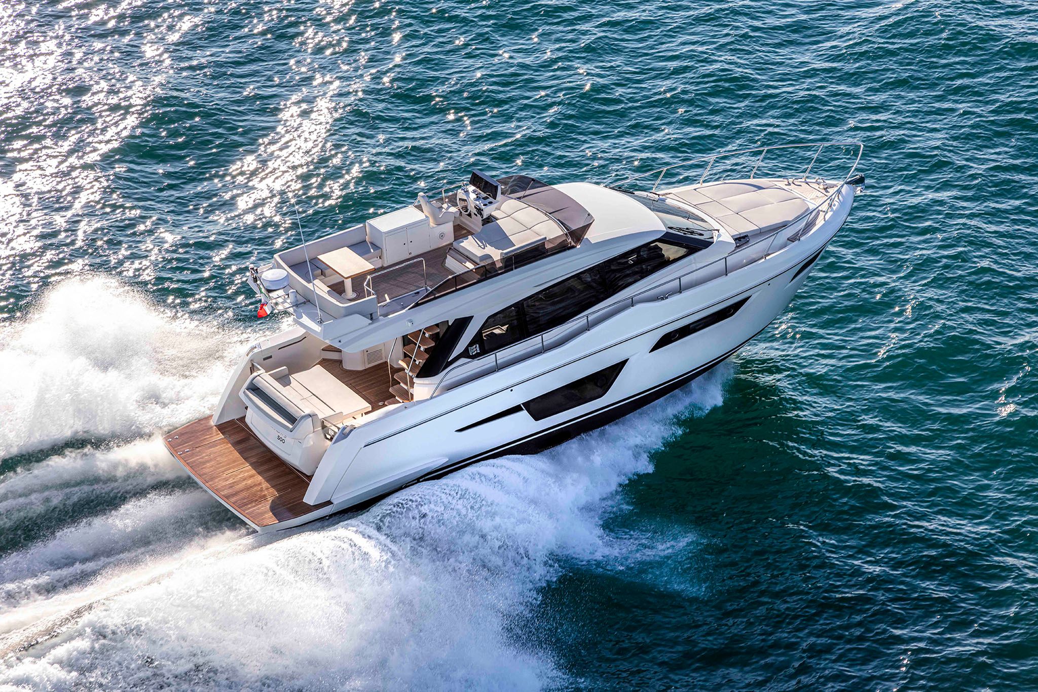 An elegant white and brown Ferretti Yachts 500 speeding through turquoise waters on a bright day.