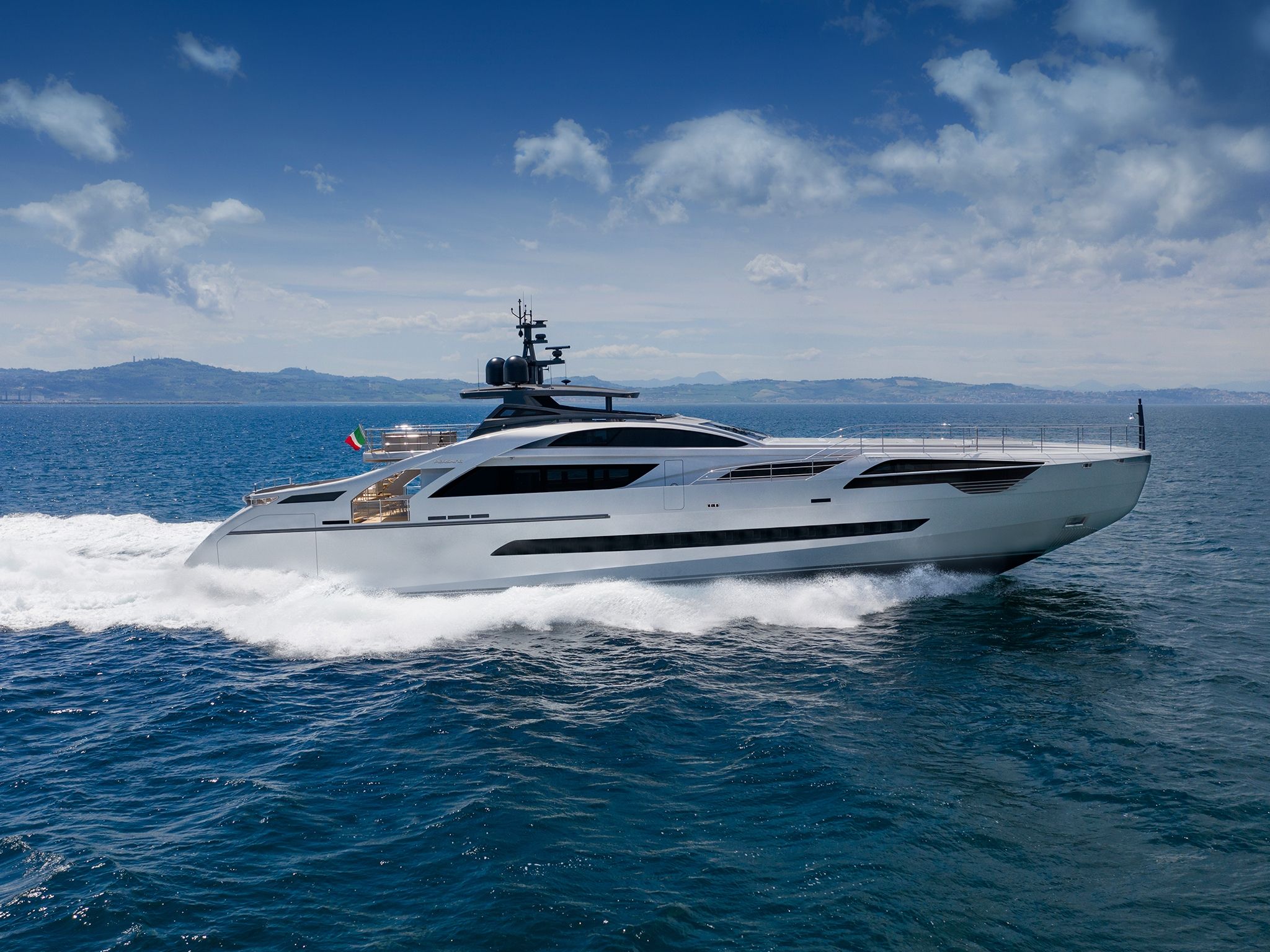 A posh looking Pershing 140 gliding smoothly across the open waters, leaving a trail of waves behind on a bright day.