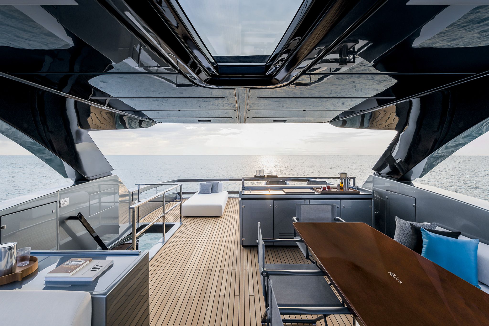 The flybridge yacht, Riva Diva 82 featuring seating, a dining area, and a view of the sea at sunset.