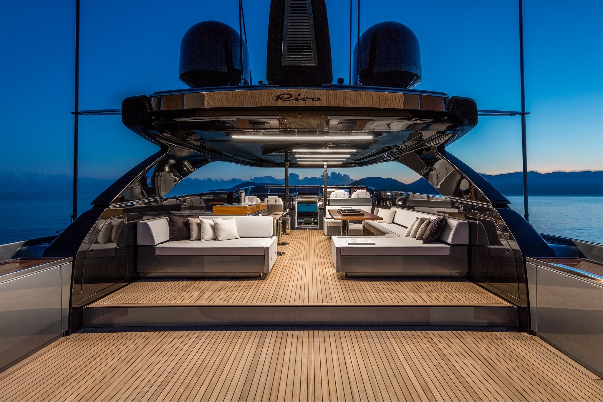 An opulent interior of the yacht, Riva 110' Dolcevita at dusk, showcasing elegant furnishing and soft orange lighting.