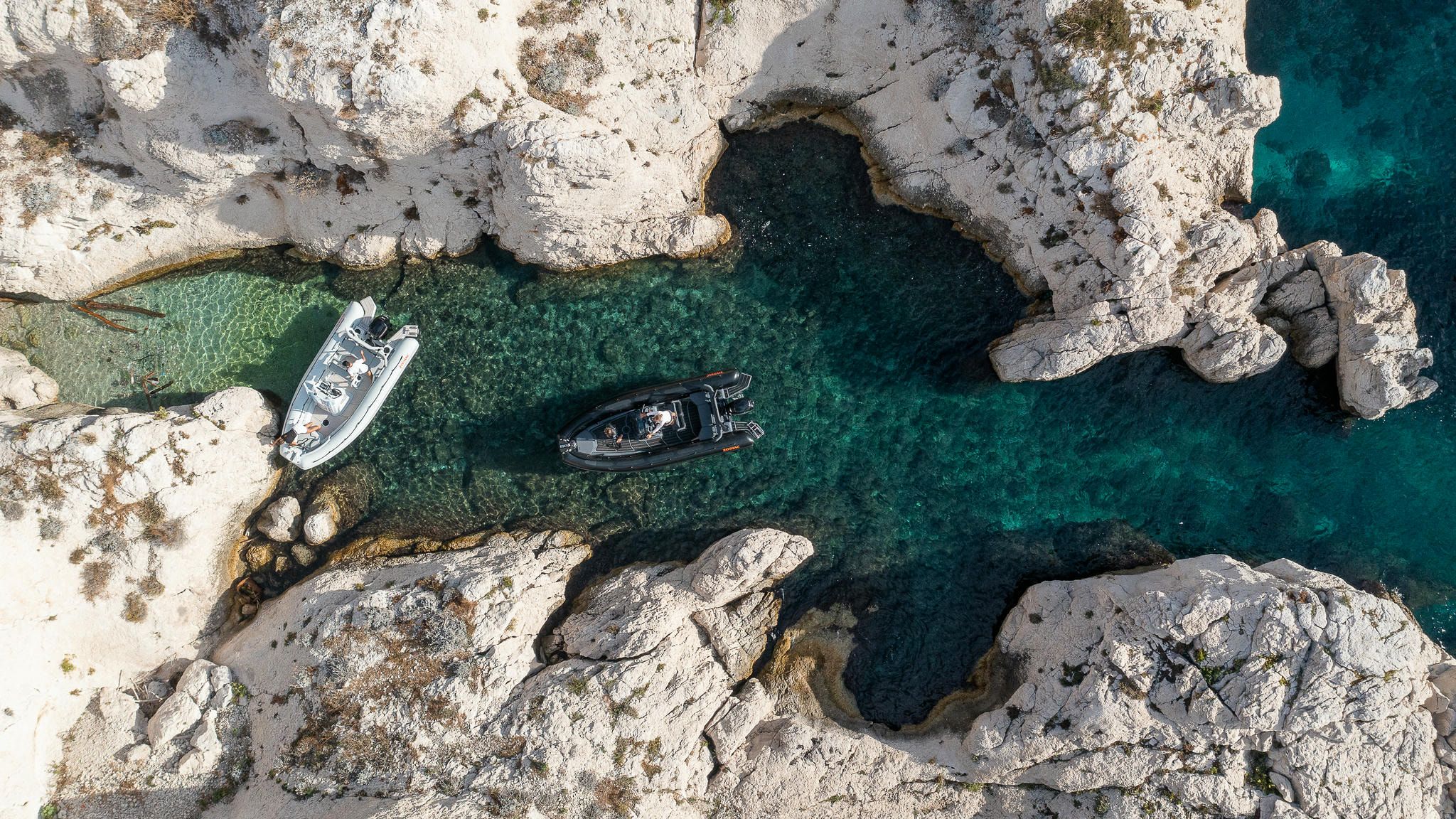 A black and white Zodiac Open Gulfstream moored in beautiful blue tranquil waters, surrounded by rocky outcrops on a bright day.