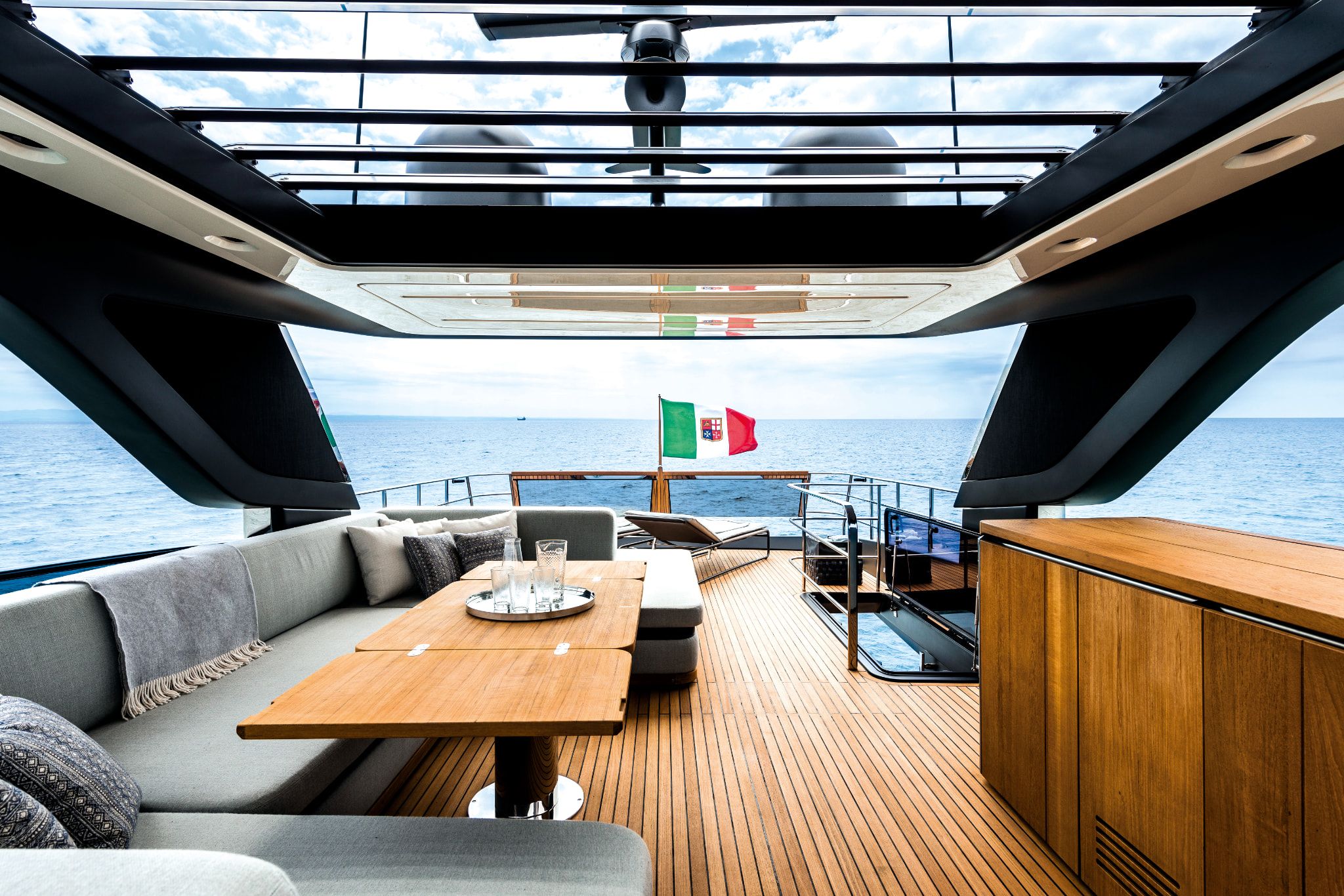 Yacht interior of Cranchi Settantotto deck with seating, dining table, and Italian flag.