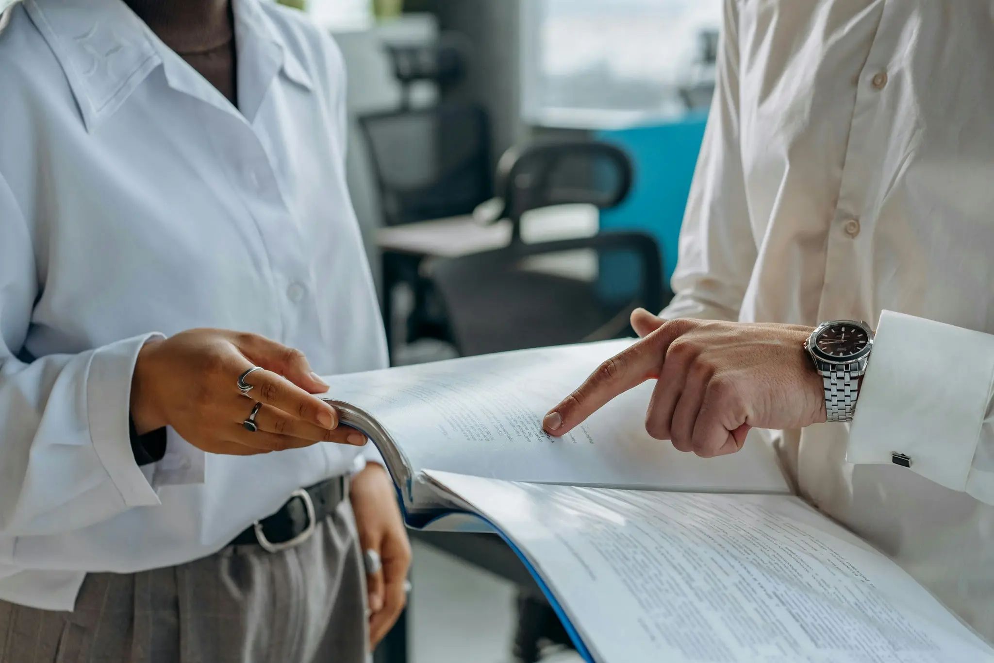 Two people holding papers, pointing and gesturing towards the contents of the paper on a business setting.