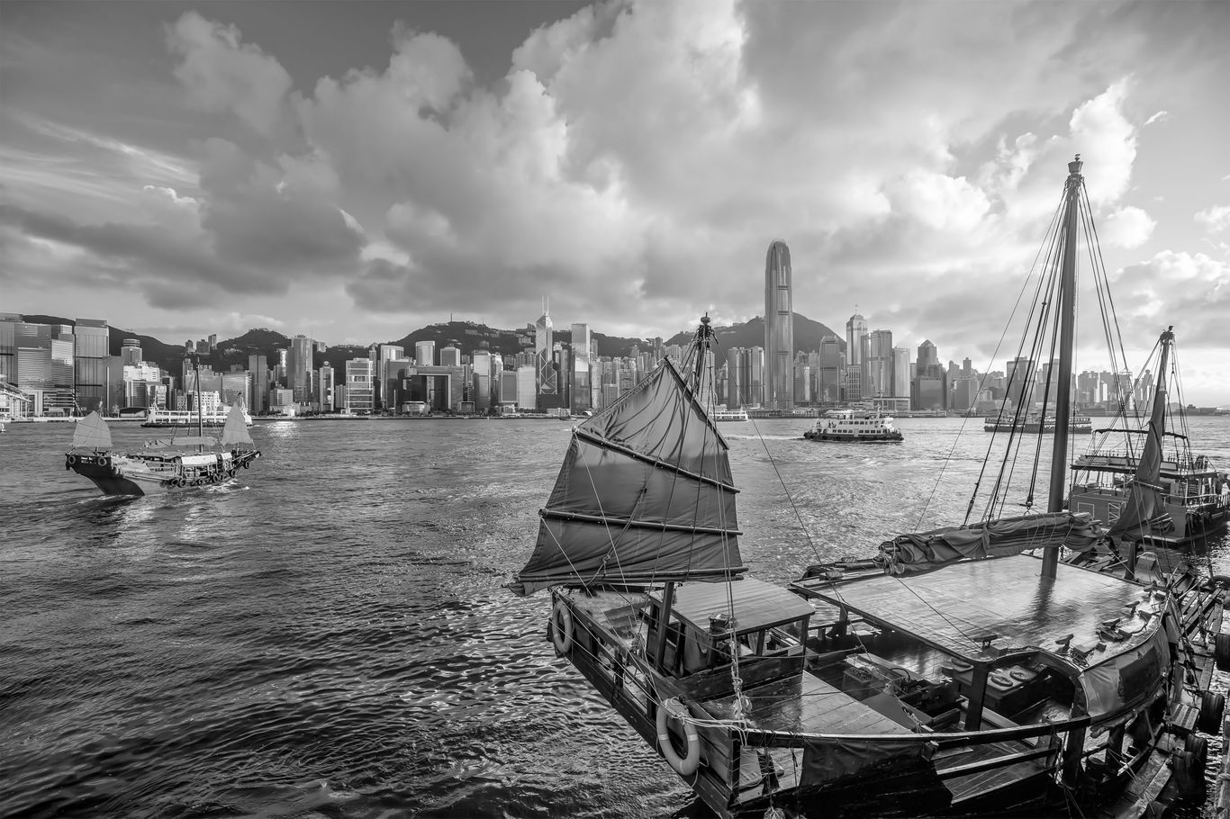 Traditional wooden junk boats in Hong Kong’s harbor with a modern skyline in the background, showcasing a blend of history and yachting culture.