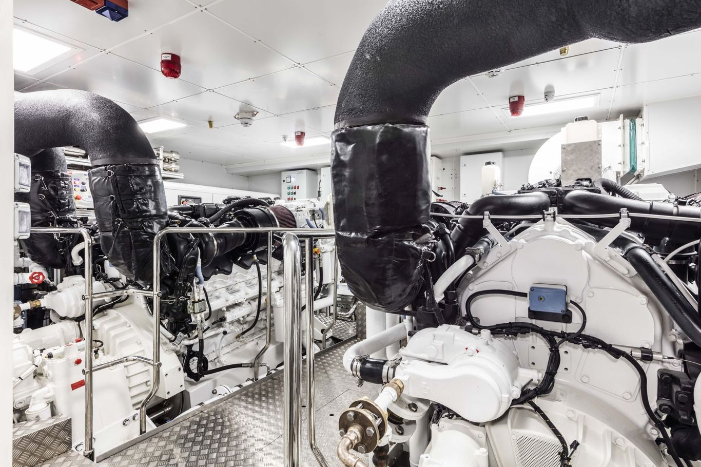Yacht engine room with powerful engines, black exhaust pipes, and a clean, organized layout.