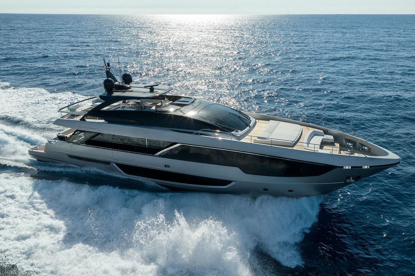 A white yacht, Riva 100 exuding grandeur of its beauty as it speeds through the sea water under a bright sky.