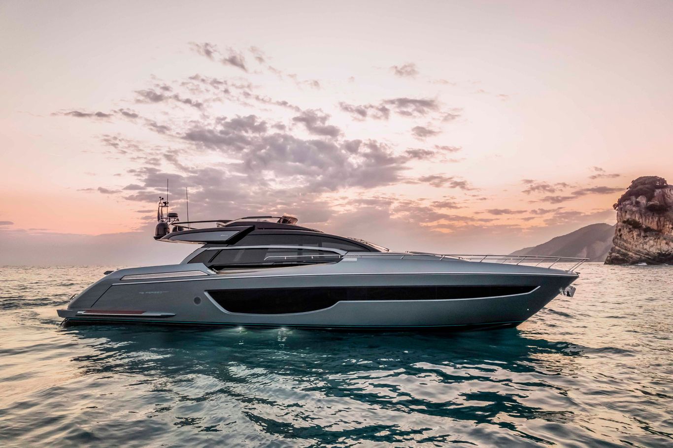 Buy yacht Hong Kong: A stunning white Riva 76' Perseo Super moored on the sea nearby some mountains during a sunset.