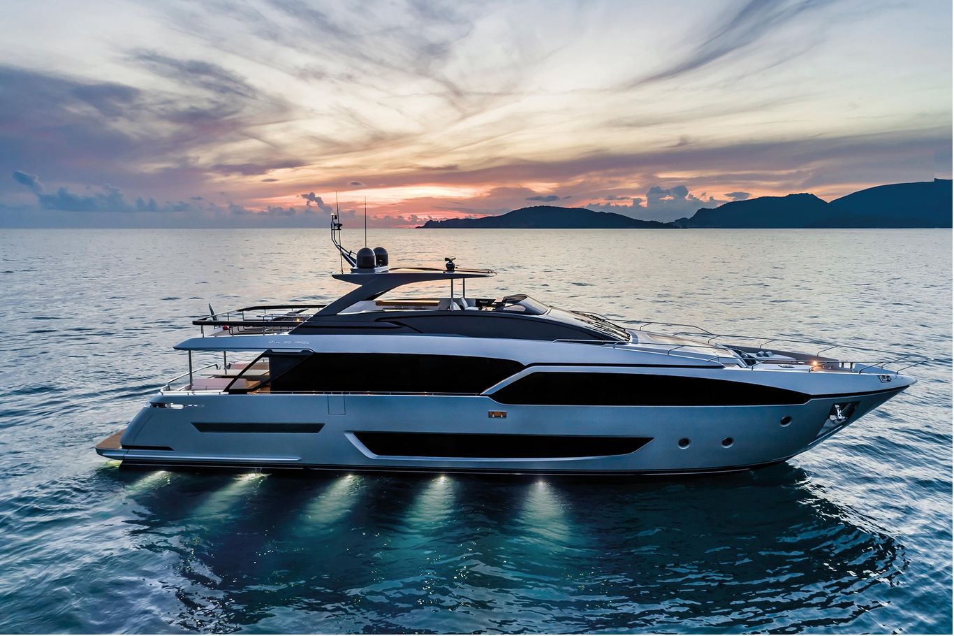 Riva Yacht: A massive white and black 90'Argo cruising beautifully during a sunset on the ocean.