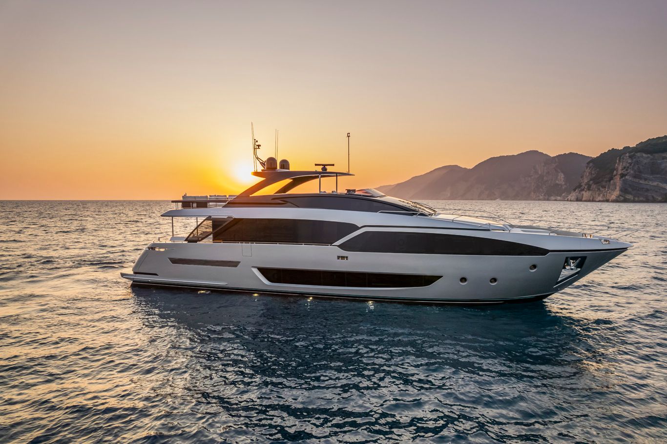 Riva Yacht: A white, sleek Riva Argo 90 sailing through the waters as the sun sets in the background.