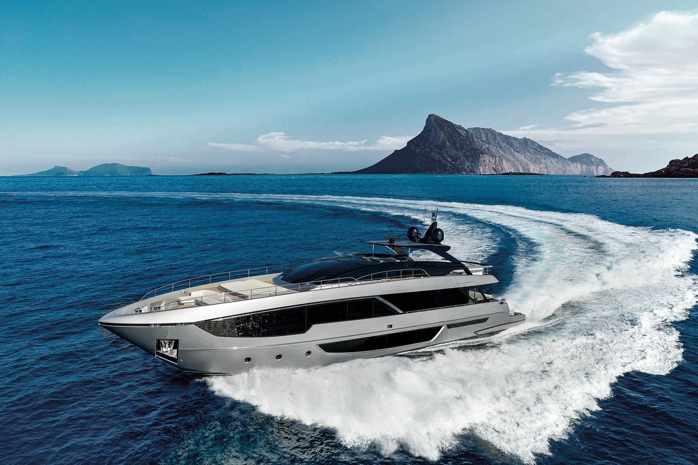 A white superyacht Riva 102' Corsaro speeding through the blue ocean waves, leaving splashes in its wake.