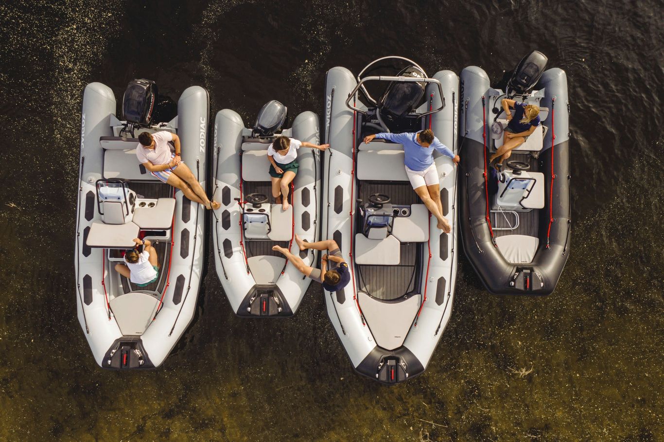 A group of individuals sitting leisurely on a line of the elegant Zodiac Open yacht tender on a sandy, brown sea.