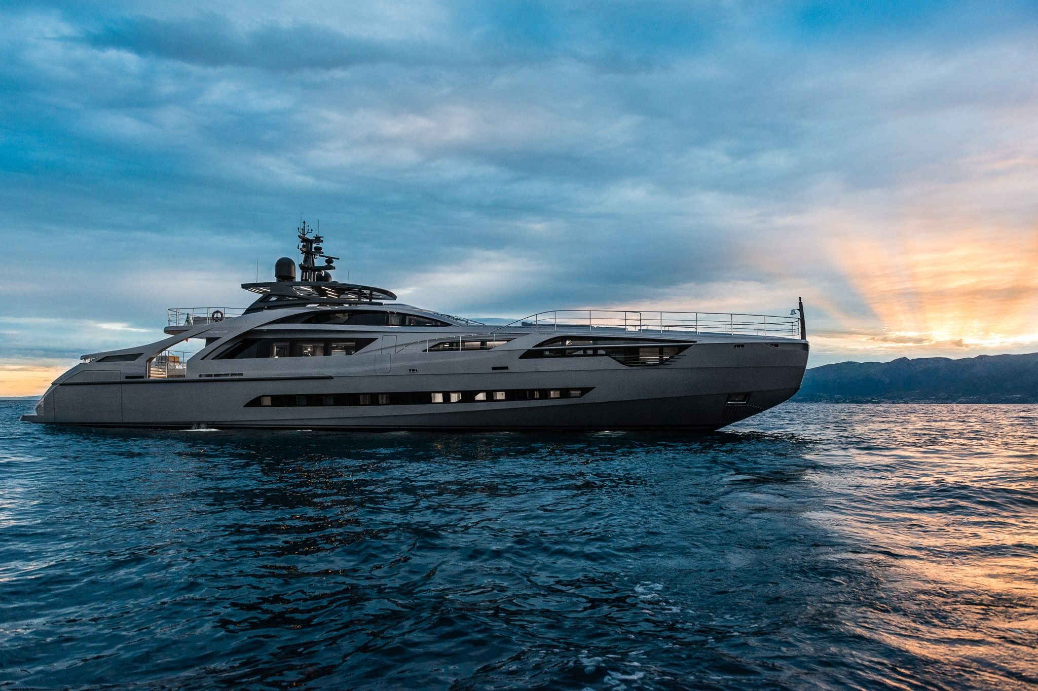 A majestic, white Pershing yacht 140 moored on the calm sea water during a sunset.