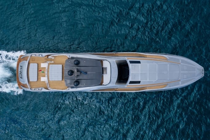 Ariel view of an elegant white and brown Pershing 140 gliding through the deep blue ocean water on a bright day.