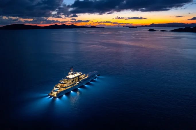 A majestic white superyacht Excellence drifts on the dark ocean, surrounded by vibrant, beautiful sunset colours.