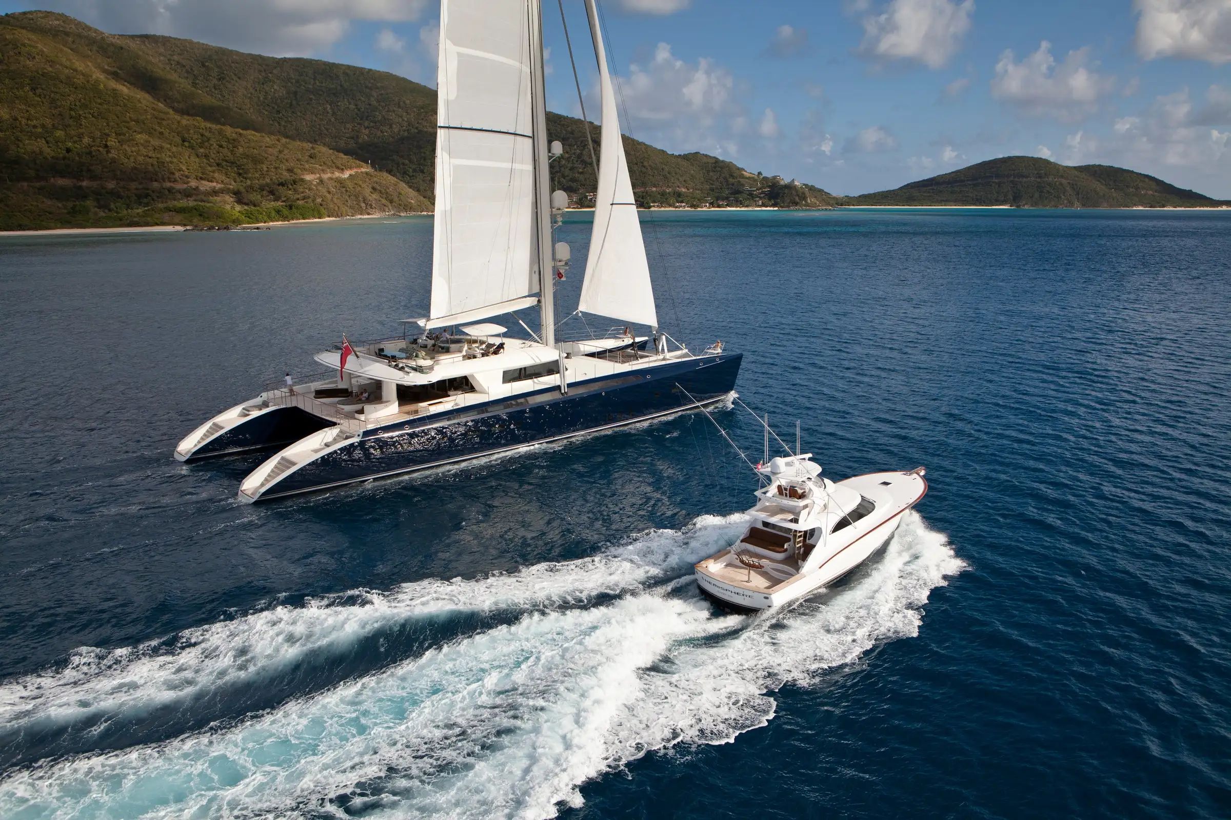 A white Superyacht HEMISPHERE sails gracefully on the ocean water alongside another yacht nearby mountains.