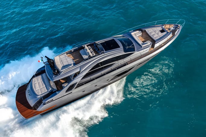 Luxurious yacht Pershing 8X with metallic gray hull and wooden decking cruising through the ocean, with waves splashing around.