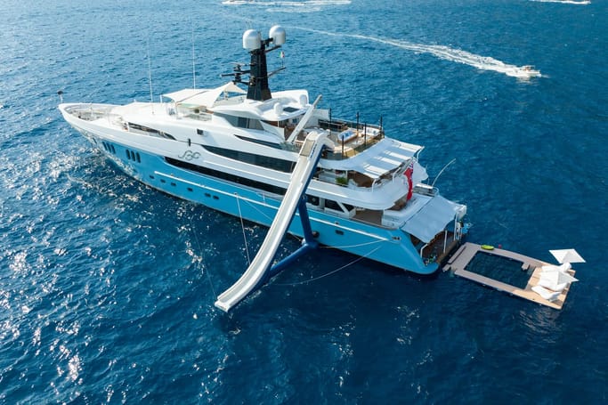 Superyacht SCOTT FREE with a light blue hull and white superstructure, featuring a water slide on the calm deep blue sea.