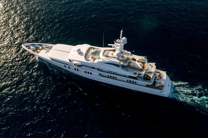 A white superyacht TALISMAN C cruising on the dark ocean water, leaving a trail of waves.