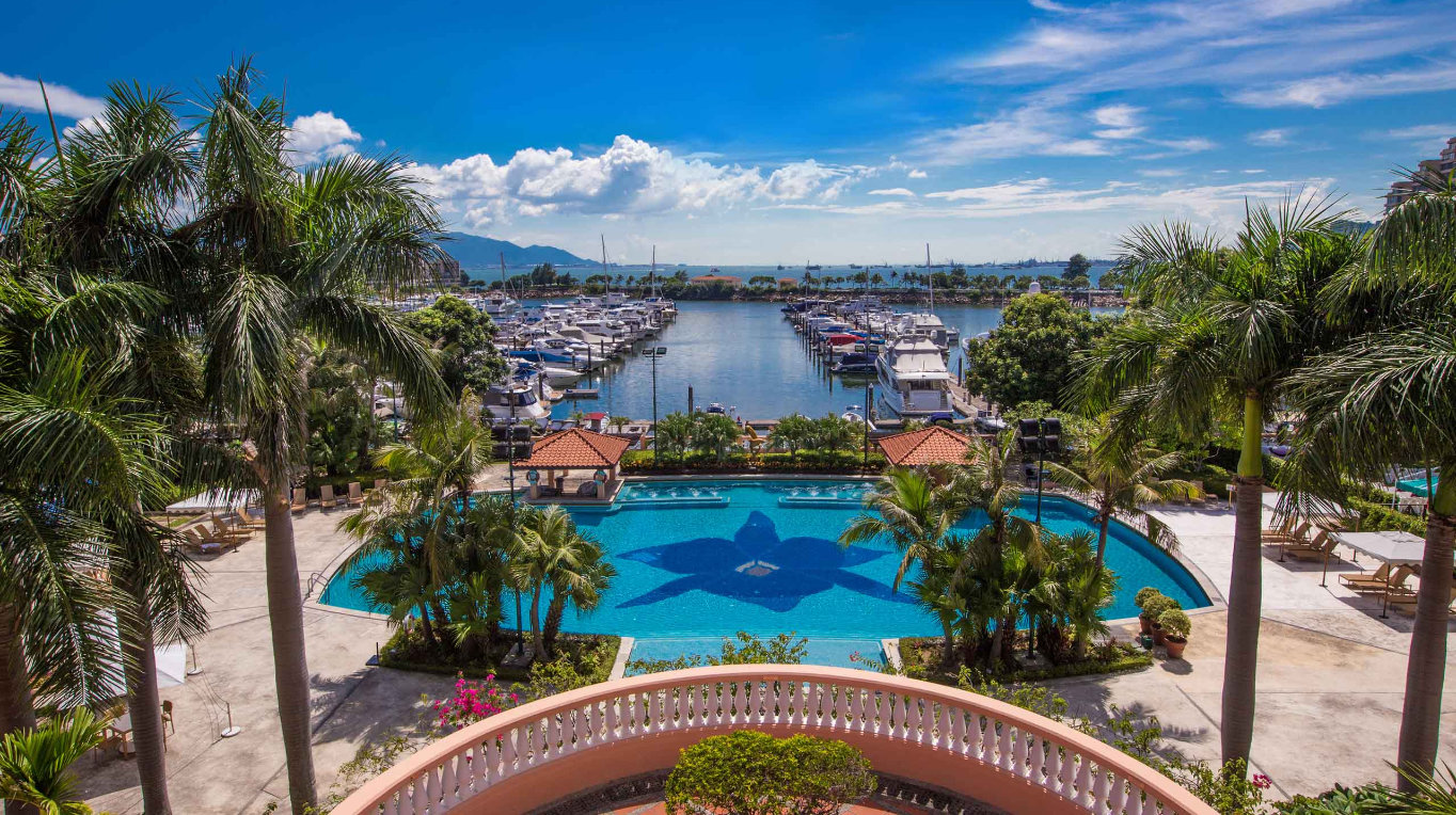 Gold Coast Marina, Hong Kong: Yachts docked with palm trees, a clear sky, and view of the clubhouse pool.