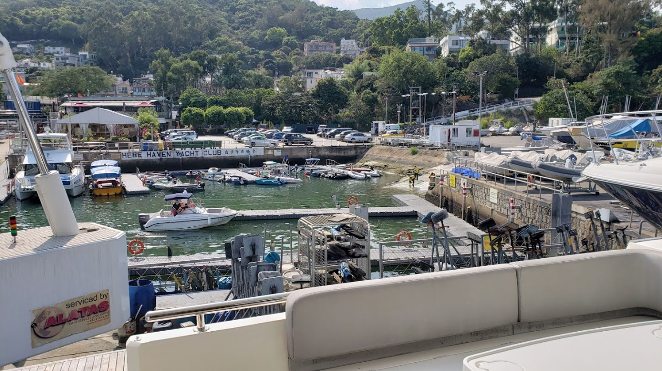 View of Hebe Haven Yacht Club with boats docked, colorful rooftops, parked cars, green water, and buildings.