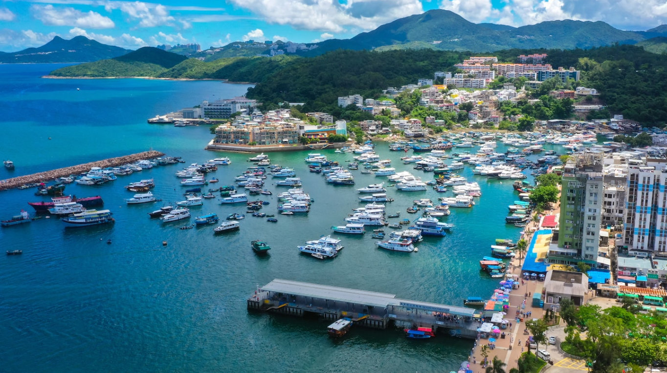 Bright aerial shot of Hong Kong Marina with numerous boats and surrounded by vibrant buildings under a clear blue sky.