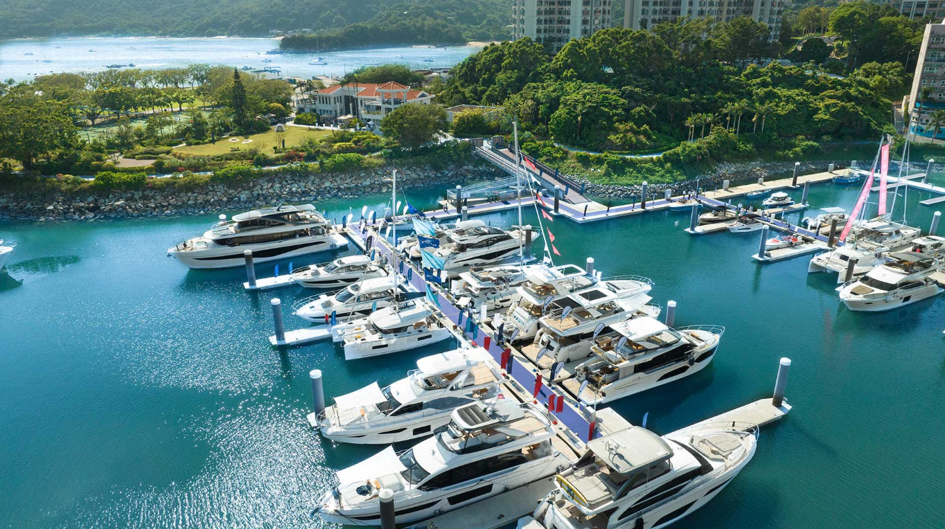 Aerial view of Lantau Yacht Club marina with docks, modern buildings, lush greenery, and mountains.