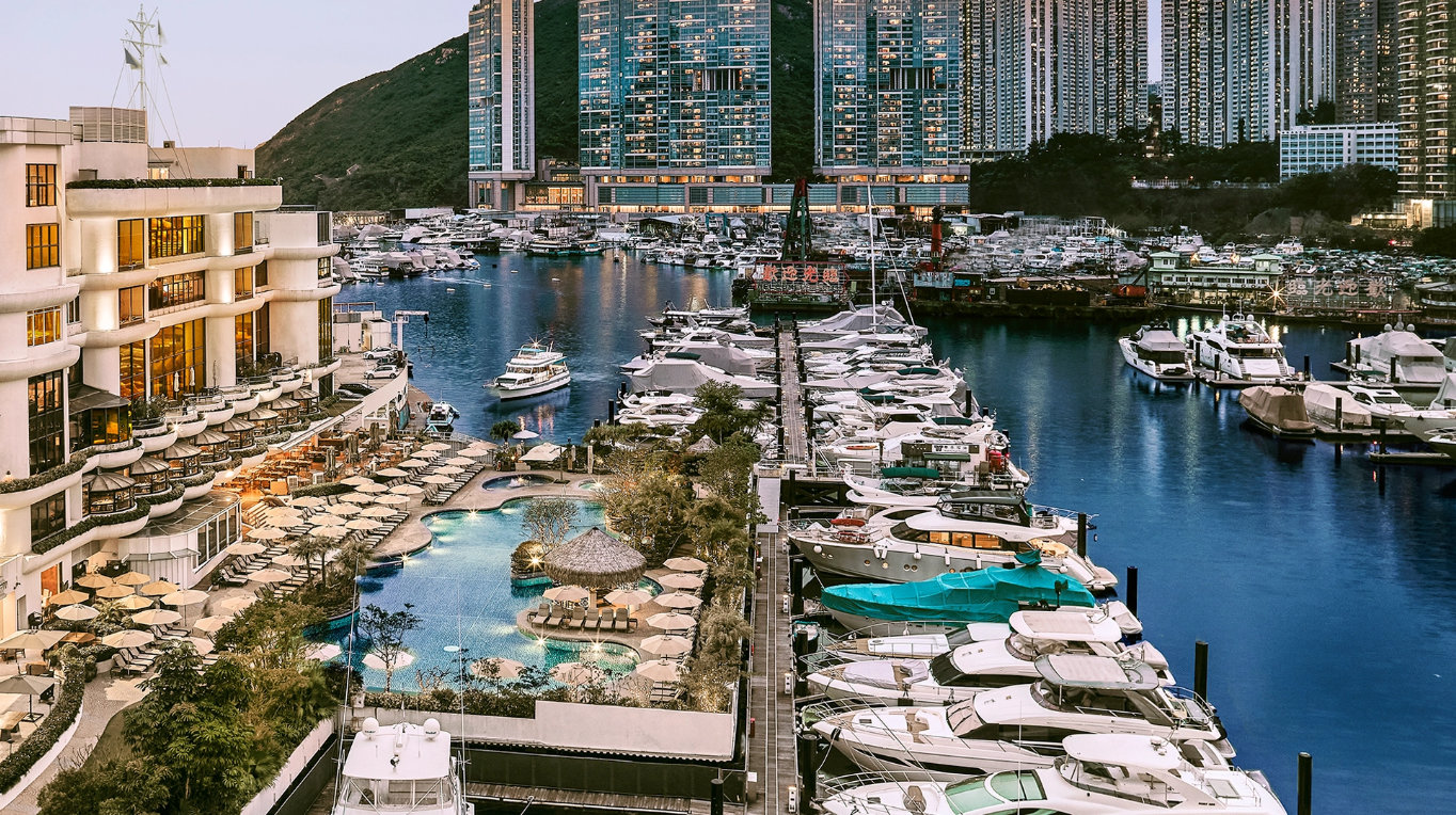 Aberdeen Marina Club luxury yachts docked, scenic waterfront, modern buildings, pool, lush greenery, and evening lights.